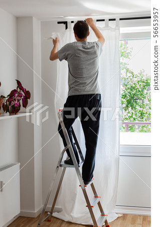 Man hangs white curtains on the curtain rod Man hangs white curtains on the curtain rod 56653957
