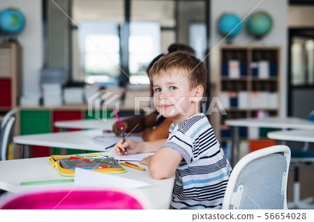 A small school boy sitting at the desk in classroom, writing. A small school boy sitting at the desk in classroom, writing. 56654028