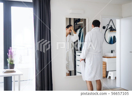Young man looking in mirror in bedroom in the morning, daily routine. Young man looking in mirror in bedroom in the morning, daily routine. 56657105