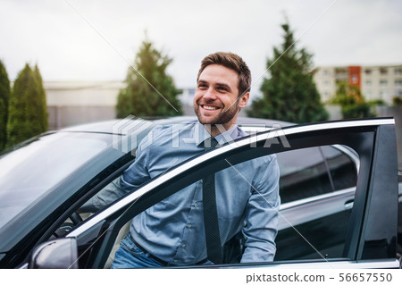Young man with blue shirt and tie getting out of car in town. Young man with blue shirt and tie getting out of car in town. 56657550