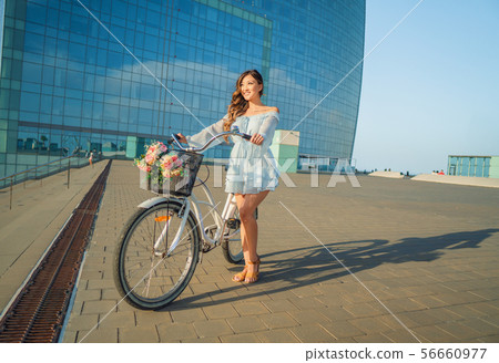 Asian model in a blue dress rides a white bicycle in a green park 56660977