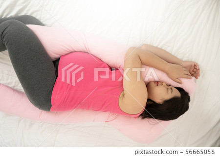 Happy pregnant woman sleeping on bed in bedroom. 56665058