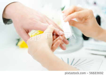 Woman filing fingernails of a man in nail parlor Woman filing fingernails of a man in nail parlor 56683692
