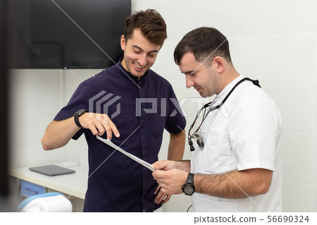 Two stomatologiests talking about results of x-ray of their patient's jaw 56690324