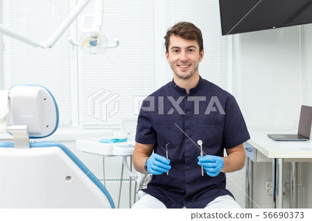 Handsome man wearing blue gloves holds dental probe and mirror in hands 56690373