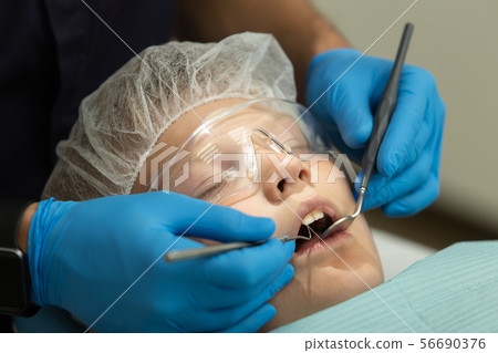 Little boy lays on dentist chair while doctor examines his teeths by probe and mirror 56690376