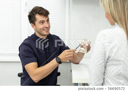 Smiling stomatologist holds pointing at model of jaw and talking with blond woman. Selective focus 56690572