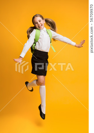 Excited Little Schoolgirl Jumping Over Yellow Studio Background. Excited Little Schoolgirl Jumping Over Yellow Studio Background. 56709970