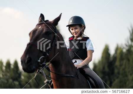 Girl teenager jockey sits on a brown horse in nature. 56716627