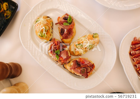 Appetizer in restaurant. Banquet concept. Bruschette with salmin and ham, decorated with basil and Appetizer in restaurant. Banquet concept. Bruschette with salmin and ham, decorated with basil and 56719231