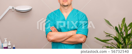 Masseur in uniforme with arms crossed standing at massage table in clinic. Copyspace for text 56732540