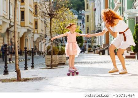 Pleased little girl standing on her skateboard Pleased little girl standing on her skateboard 56733484