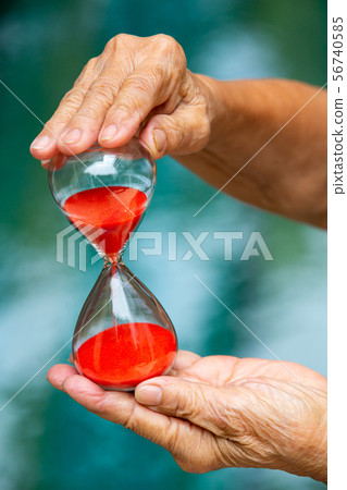 Senior woman's hands holding red hourglass in blue 56740585