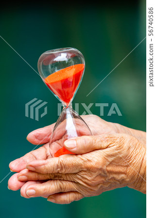 Senior woman's hands holding red hourglass in blue 56740586