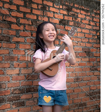 Little asian child play the ukulele, old brick 56744262