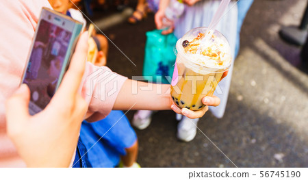 [Harajuku culture image] A scene where a hipster girl buys tapioca milk tea and posts it on an SNS via smartphone 56745190