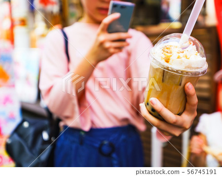[Harajuku culture image] A scene where a hipster girl buys tapioca milk tea and posts it on an SNS via smartphone 56745191