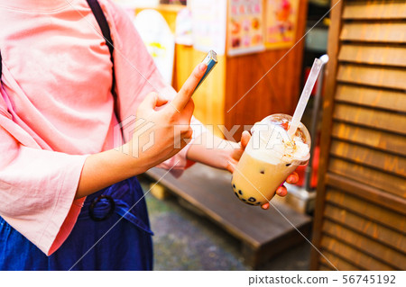 [Harajuku culture image] A scene where a hipster girl buys tapioca milk tea and posts it on an SNS via smartphone 56745192