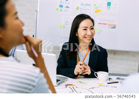 Asian mature business woman smiling and looking at other business people while sitting in meeting 56746545
