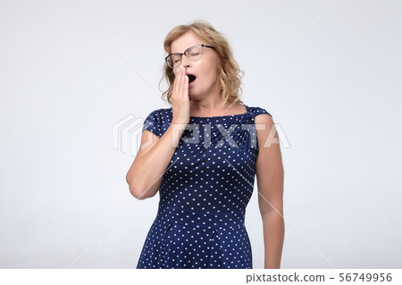 Senior caucasaian woman yawning, having sleepy expression, covers mouth with palm 56749956