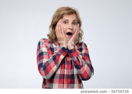 Amazed senior woman holding hands near face being astonished Amazed senior woman holding hands near face being astonished 56750726