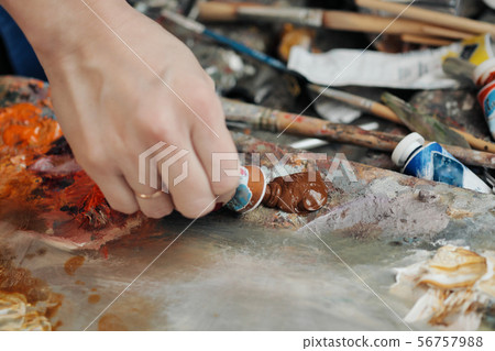 A woman artist squeezes oil paint onto a palette from a tube. A woman artist squeezes oil paint onto a palette from a tube. 56757988