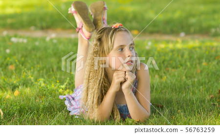 Beautiful young blonde girl lying on a field, green grass. Outdoors Enjoy Nature. Healthy Smiling Beautiful young blonde girl lying on a field, green grass. Outdoors Enjoy Nature. Healthy Smiling 56763259