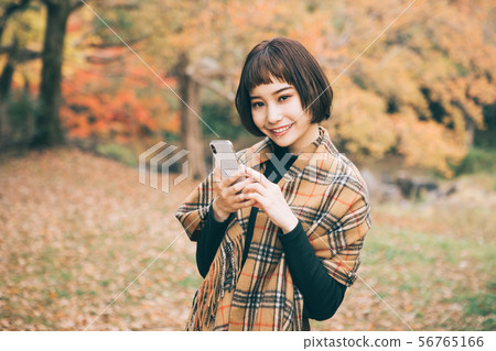 A woman who touches a smartphone surrounded by autumn leaves A woman who touches a smartphone surrounded by autumn leaves 56765166