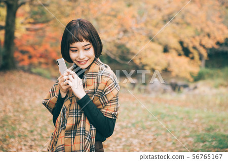 接觸由秋葉包圍的智能手機的婦女 接觸由秋葉包圍的智能手機的婦女 56765167