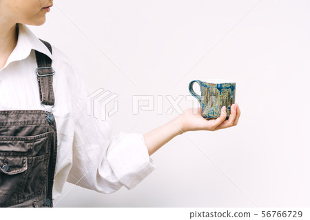 Woman with a blue ceramic mug in hand on a background of a white wall Woman with a blue ceramic mug in hand on a background of a white wall 56766729