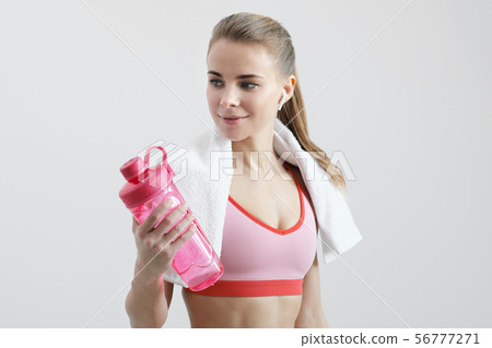 Sporty blonde girl with a white towel around her neck, in red sportswear and with white wireless 56777271