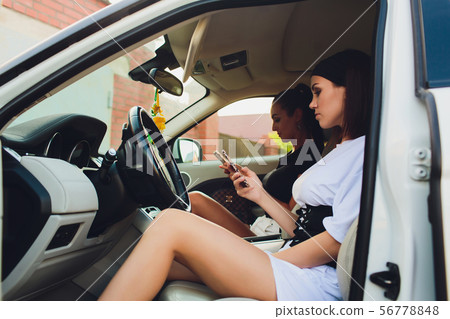 Beautiful woman smiling while sitting on the passenger seats in the car. Girl is using a smartphone. Beautiful woman smiling while sitting on the passenger seats in the car. Girl is using a smartphone. 56778848
