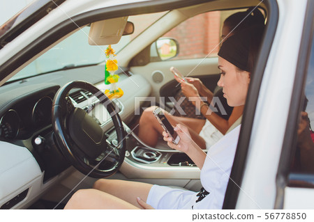 Beautiful woman smiling while sitting on the passenger seats in the car. Girl is using a smartphone. 56778850