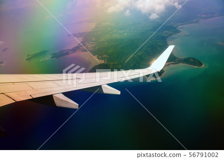 Wing of airplane in cloudy sky with rainbow effect 56791002