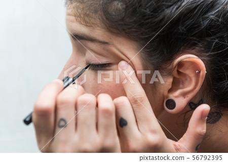 Young woman applies eyeliner to her eye in the bathroom. Young woman applies eyeliner to her eye in the bathroom. 56792395