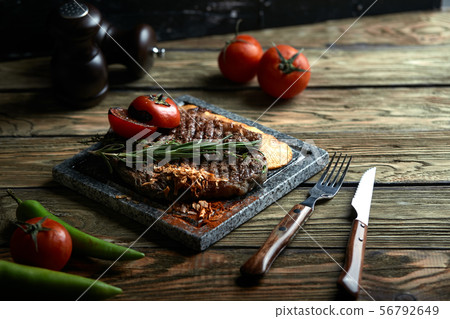 Grilled steak with knife and fork carved on black stone slate. Steak on a hot marble stone. Copy 56792649