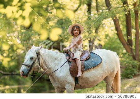 Little baby boy with curly hair dressed as hobbit playing with horse in summer forest 56796903