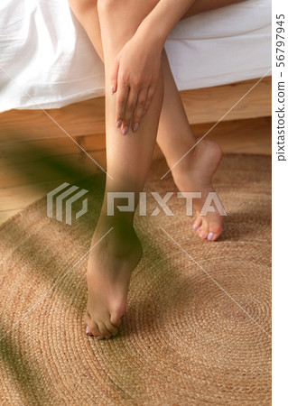 Young woman sitting on bed and touching her leg 56797945