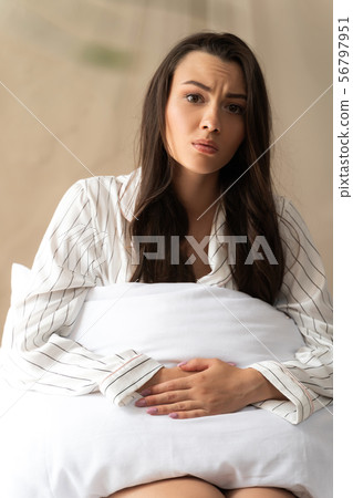 Unhappy young woman sitting on bed and having stomachache 56797951