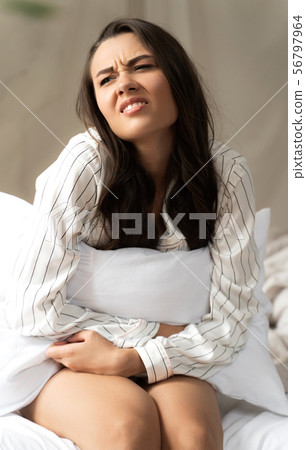 Displeased young woman sitting on bed and having stomachache 56797964