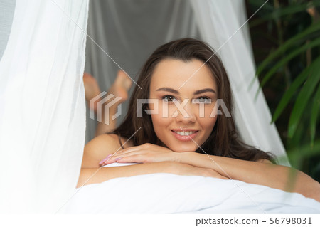 Charming young woman lying down on bed and smiling Charming young woman lying down on bed and smiling 56798031