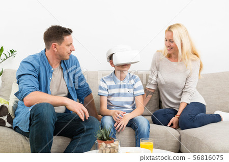 Happy family at home on living room sofa having fun playing games using virtual reality headset Happy family at home on living room sofa having fun playing games using virtual reality headset 56816075