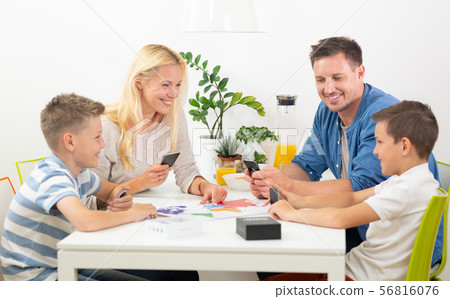 Happy young family playing card game at dining table at bright modern home. Happy young family playing card game at dining table at bright modern home. 56816076