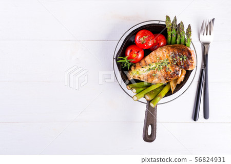 Grilled chicken breast on a cast iron skillet with grill vegetables on a wooden background, flat lay 56824931