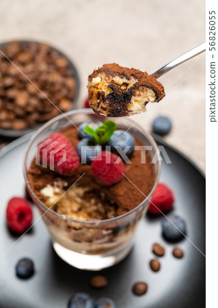 Classic tiramisu dessert portion with blueberries and raspberries in a glass cup on concrete Classic tiramisu dessert portion with blueberries and raspberries in a glass cup on concrete 56826055