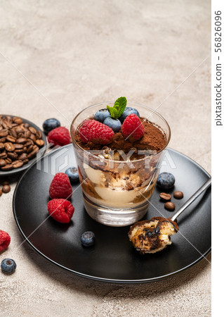 Classic tiramisu dessert portion with blueberries and raspberries in a glass cup on concrete 56826096