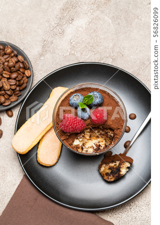 Classic tiramisu dessert portion with blueberries and raspberries in a glass cup on concrete Classic tiramisu dessert portion with blueberries and raspberries in a glass cup on concrete 56826099