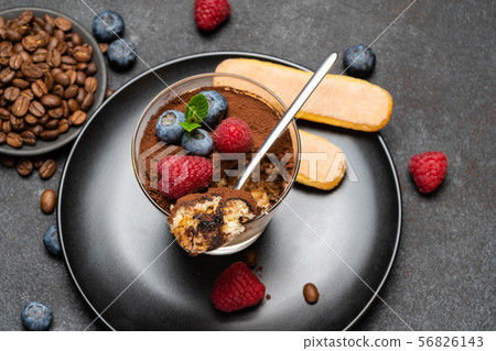 Classic tiramisu dessert portion with blueberries and raspberries in a glass cup on stone serving Classic tiramisu dessert portion with blueberries and raspberries in a glass cup on stone serving 56826143