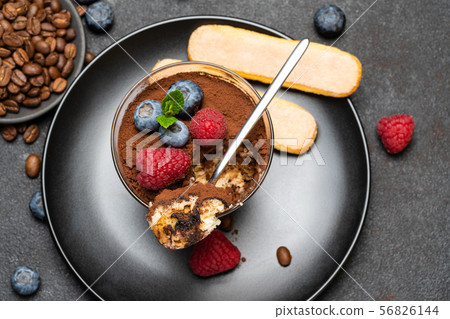 Classic tiramisu dessert portion with blueberries and raspberries in a glass cup on stone serving Classic tiramisu dessert portion with blueberries and raspberries in a glass cup on stone serving 56826144