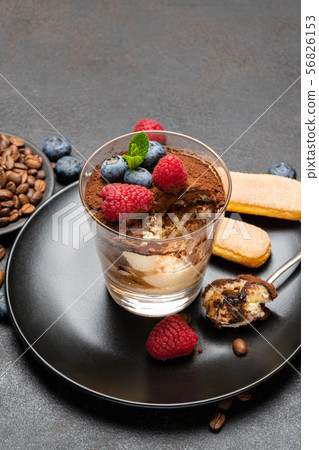 Classic tiramisu dessert portion with blueberries and raspberries in a glass cup on stone serving 56826153